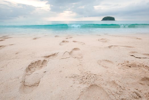 Footprints on beautiful sandy beach and turquoise sea water at sunset time.