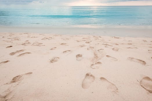 Footprints on beautiful sandy beach and turquoise sea water at sunset time.