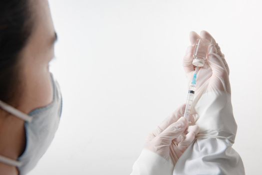 Medication nurse wearing protective gloves and white scrubs get a needle or shot ready for an injection.