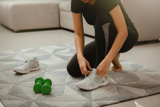 Woman getting ready for workout at home. She is tying shoelace on sneakers. Sport and recreation concept.
