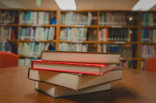 Stack of books on table and blurred bookshelf in the library room, education background.