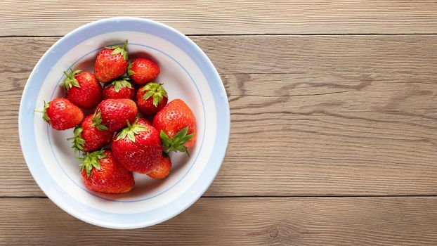 Natural ripe strawberries in a plain white bowl on a wooden background. Top view, copyspace.
