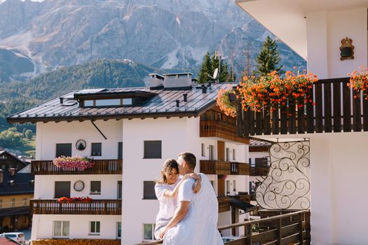 A guy and a girl cuddle with a blanket outside a hotel in mountains. Cortina Ampezzo is an Italian city in province of Belluno in Veneto region, a winter resort in Dolomites