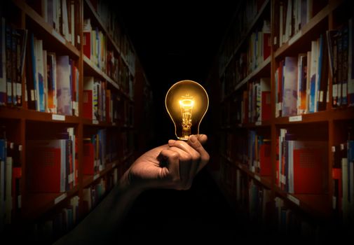 Hand holding a light bulb with bookshelf in library background. Concept The idea of reading books, knowledge, and searching for new ideas.