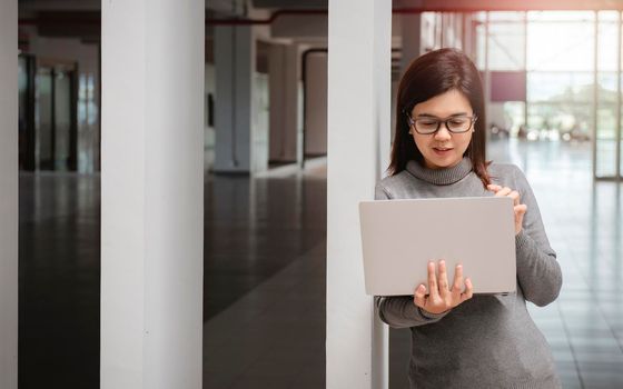 Woman in office has video conversation. Young positive woman in glasses standing in front of laptop and talking with somebody online.