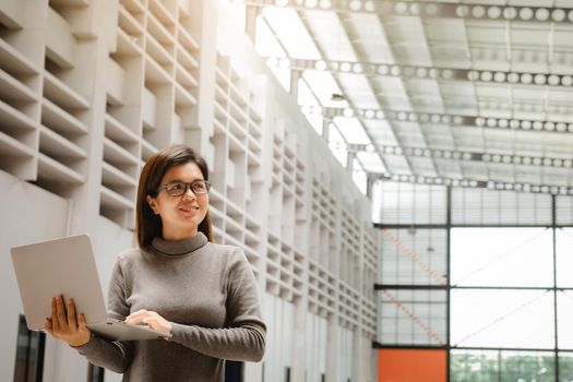 Portrait of positive woman executive holding a laptop standing in office. Smiling business woman in casuals at office.