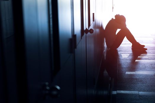 Silhouette of depressed man sitting on walkway of building. Sad man, Cry, drama, lonely and unhappy concept.