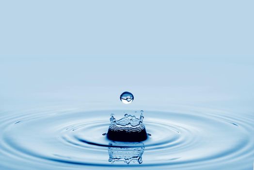 Water splash in dark blue color with a drop of water flying from above