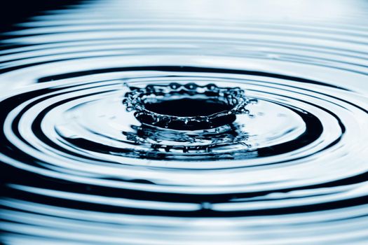 Water splash in dark blue color with a drop of water flying from above.