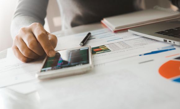 Businesswoman analyze business report graph and finance chart using smartphone and computer laptop at corporate office.