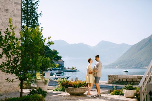 A man and a woman stand hugging in Perast on the shore of the Bay of Kotor and look at each other . High quality photo