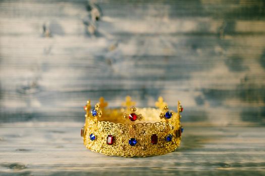 Golden crown encrusted with precious stones for wedding in the church, against a wooden background
