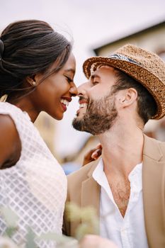 A close-up of portraits of an African-American bride and Caucasian groom in a straw hat. Interracial wedding couple. Wedding in Florence, Italy.