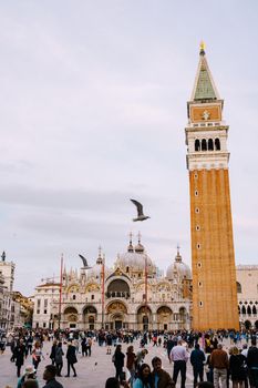 A huge bell tower made of red brick in Piazza San Marco in Venice, Italy. Against background of a cloudy, evening, October sunset sky.