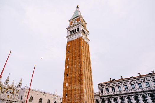 A huge bell tower made of red brick in Piazza San Marco in Venice, Italy. Against background of a cloudy, evening, October sunset sky.