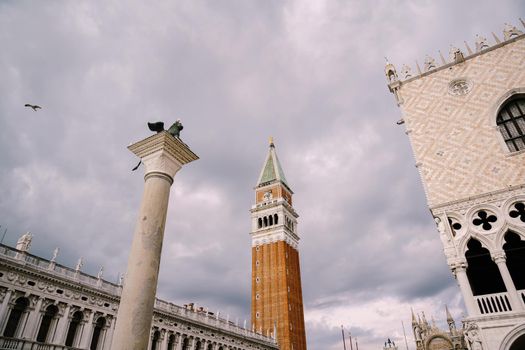 A huge bell tower made of red brick in Piazza San Marco in Venice, Italy. Against background of a cloudy, evening, October sunset sky.