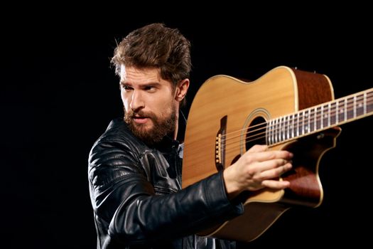 A man with a guitar in his hands leather jacket music performance rock star modern style dark background. High quality photo