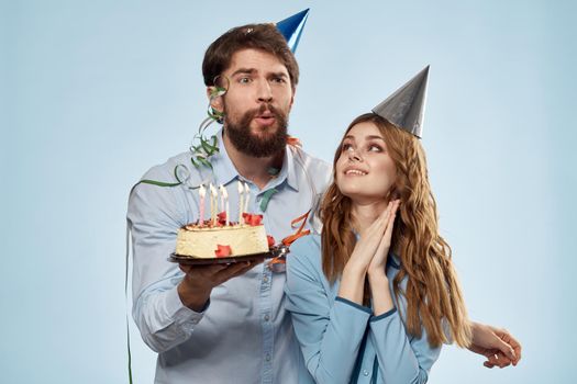 man and woman celebrate birthday with cake and in hats on blue background. High quality photo