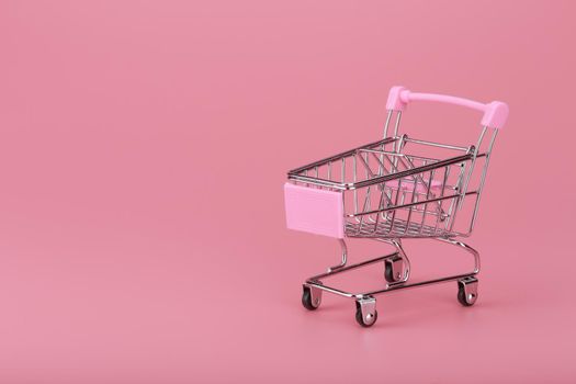 Shopping cart against pink background with copy space. Concept of online shopping and commerce. High quality photo