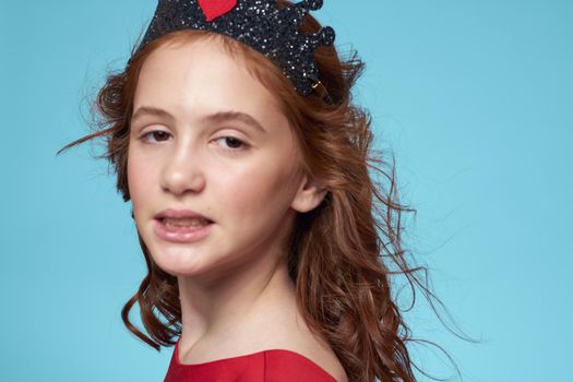 little girl with curly hair with a crown on her head red dress Smile blue background. High quality photo