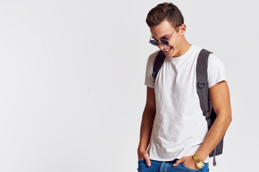 man in sunglasses with a backpack on his back and in a white t-shirt on a light background cropped view of emotion. High quality photo