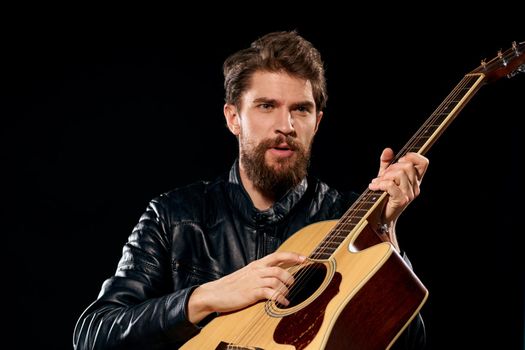 A man with a guitar in his hands leather jacket music performance rock star modern style dark background. High quality photo