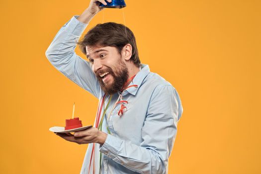Cheerful man with a cake on a yellow background birthday holidays cap on his head. High quality photo