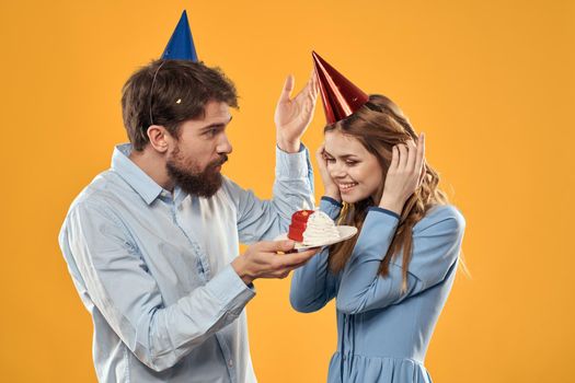 Birthday party man and woman in a cap with a cake on a yellow background cropped view. High quality photo