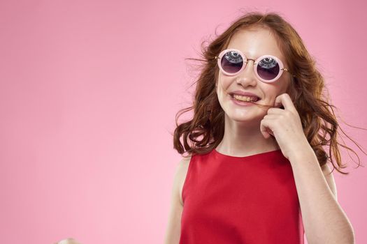 Girl with curly hair dark round glasses fun red dress pink background. High quality photo