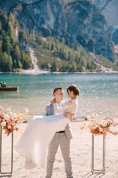 The groom circles the bride in her arms at the venue for the ceremony, with two autumn floral columns instead of an arch, against the backdrop of Lago di Braies in Italy