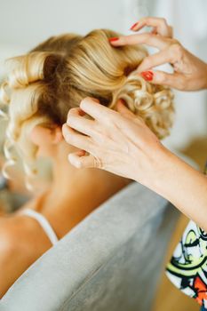 The stylist fixes the styling for a woman with long blond hair using hairspray . High quality photo