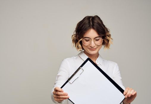Happy woman in glasses holds a folder with a white sheet of mockup paper. High quality photo