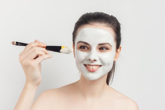 brunette naked shoulders face cream brush in hand. High quality photo
