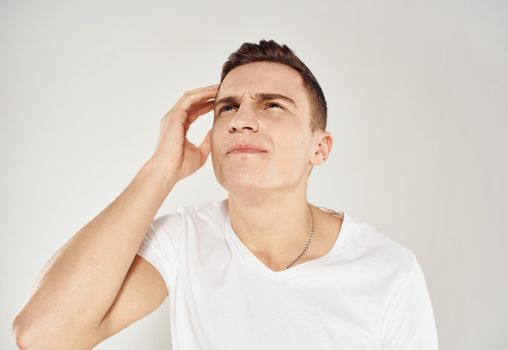 Pensive man in a white T-shirt touches his face with his hand on a light background portrait of a model. High quality photo