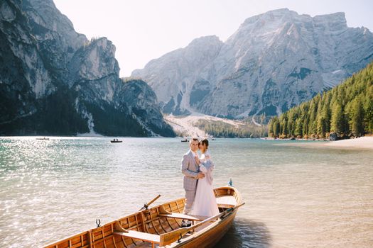 Bride and groom sailing in wooden boat, with oars at Lago di Braies lake in Italy. Wedding in Europe - Newlyweds are standing embracing in boat