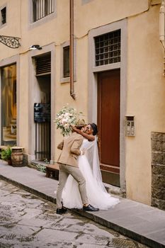 African-American bride and Caucasian groom kiss on the street. Interracial wedding couple. Wedding in Florence, Italy