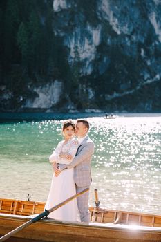 Bride and groom sailing in wooden boat, with oars at Lago di Braies lake in Italy. Wedding in Europe - Newlyweds are standing embracing in boat