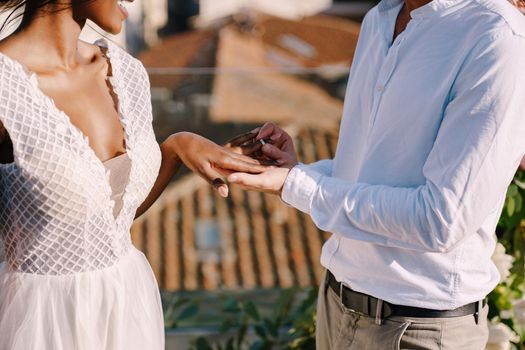 Interracial wedding couple - African-American bride and Caucasian groom. Groom puts a ring on brides finger. Destination fine-art wedding in Florence, Italy. Wedding ceremony on the roof of building