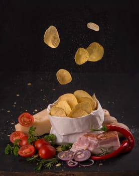 Potato chips on a dark wooden board. Fast food. Dark background. Top view