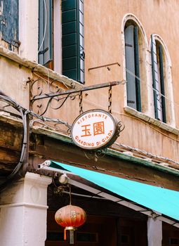 Close-ups of building facades in Venice, Italy. An ancient sign of a Chinese restaurant in Venice. Oval metal on a metal chain with forged elements.