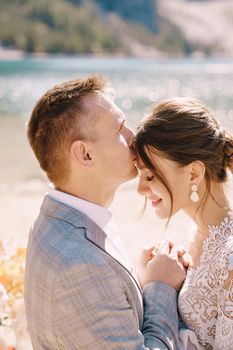 Newlyweds kiss on the spot for the ceremony, with an arch of autumn flower columns, against the backdrop of Lago di Braies in Italy. Destination wedding in Europe, at Braies lake.