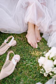 Wedding in Florence, Italy, in an old villa-winery. Barefoot legs of the bride on the grass, next to shoes and bouquet.