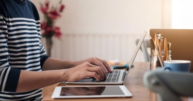 Close up young casual man sitting at desk studying on laptop happy at the coffee shop.