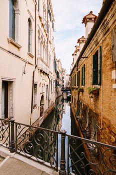 Beautiful narrow canal in Venice, Italy. Small stone bridge connects houses from both sides of the canal. Building facades are aged by weather and water.
