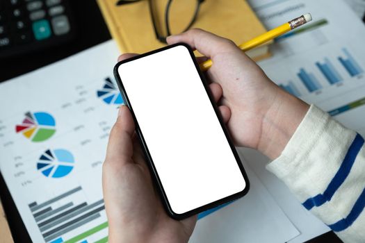 Top view of woman holding blank screen smartphone in dark trendy workspace for accounting financial.