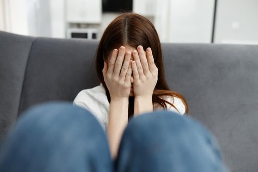 woman covers her face with her hands but feeling unwell at home sitting on the couch. High quality photo