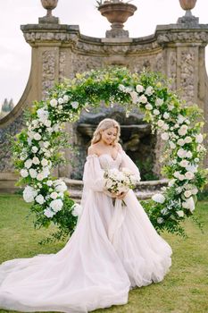 Portrait of the bride near the round arch of flowers. The scenery of the wedding ceremony. Wedding at an old winery villa in Tuscany, Italy.