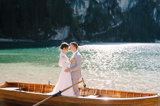 Bride and groom sailing in wooden boat, with oars at Lago di Braies lake in Italy. Wedding in Europe - Newlyweds are standing embracing in boat