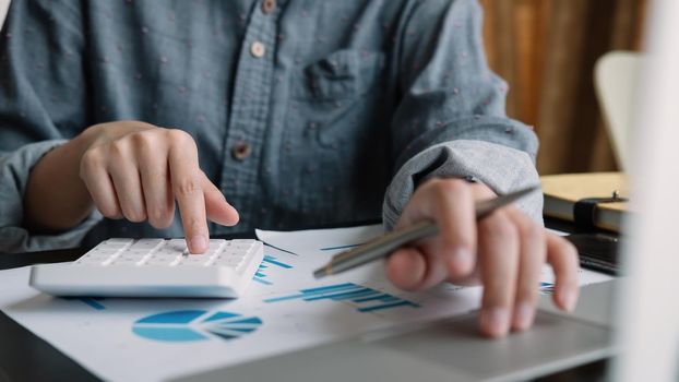 Business woman or accountant working on calculator and laptop computer with financial document, graph diagram and calculator on office table, work from home concept