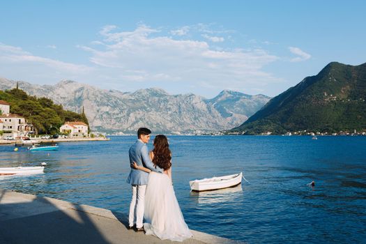 The bride and groom embracing on the pier near the old town of Perast, next to them is a boat . High quality photo